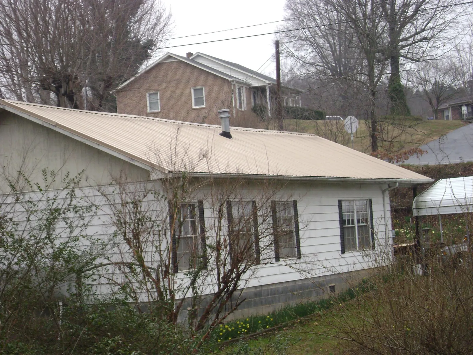 Tan metal roof on a white sided house set into a hillside — Commercial Roofing by Roofing Brothers in Davis